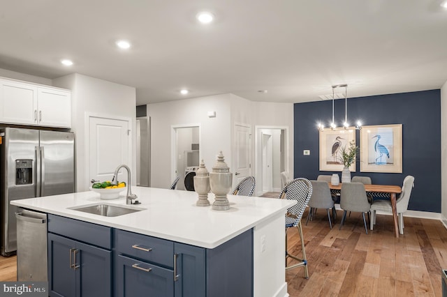 kitchen featuring pendant lighting, a kitchen island with sink, white cabinets, sink, and light hardwood / wood-style floors