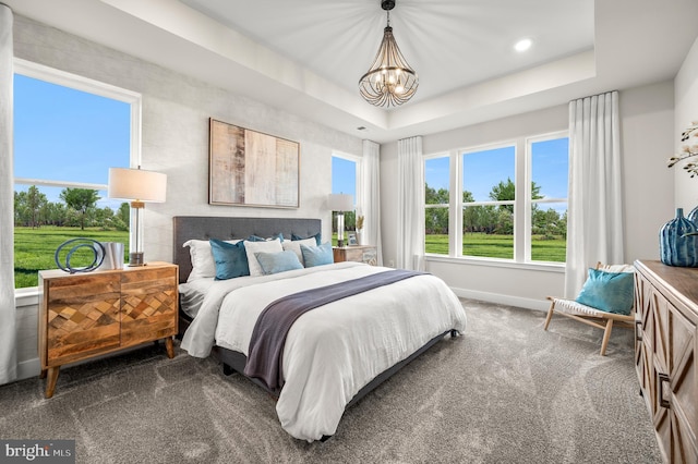 carpeted bedroom featuring a tray ceiling, multiple windows, and an inviting chandelier