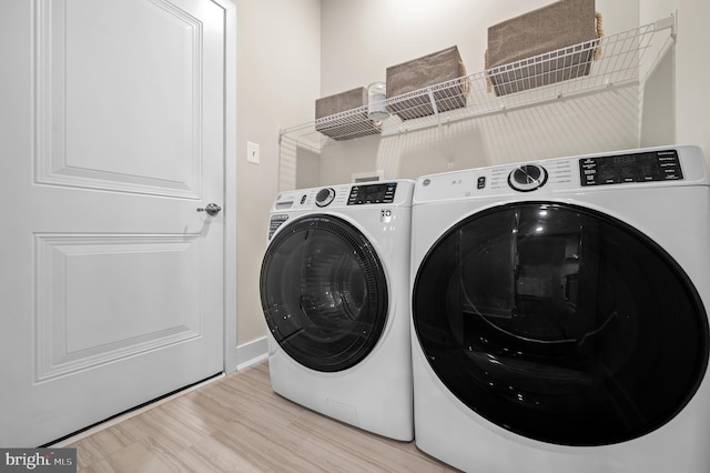 clothes washing area with washing machine and dryer and light hardwood / wood-style floors