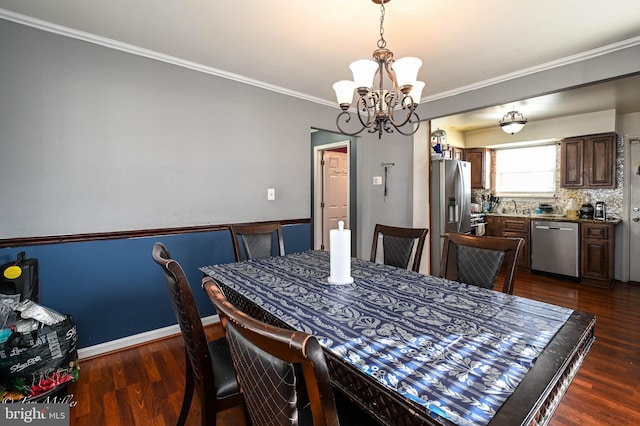 dining area with sink, dark hardwood / wood-style flooring, ornamental molding, and an inviting chandelier