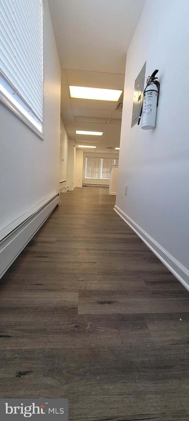 corridor with dark hardwood / wood-style flooring, a drop ceiling, and a baseboard heating unit