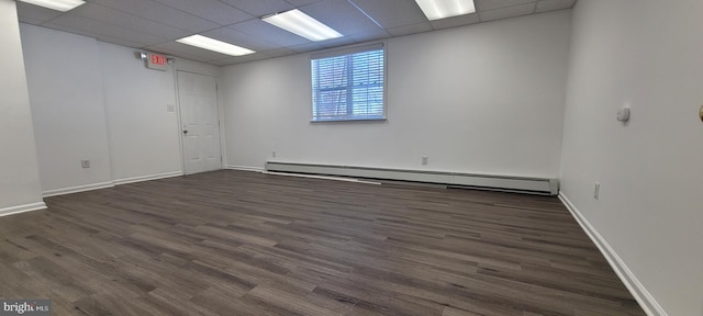 empty room with a paneled ceiling, dark hardwood / wood-style flooring, and baseboard heating