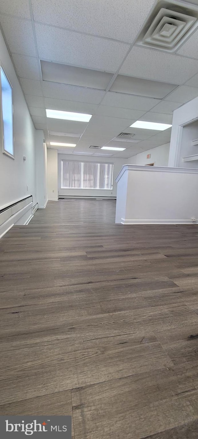 unfurnished room featuring dark hardwood / wood-style flooring, baseboard heating, and a paneled ceiling