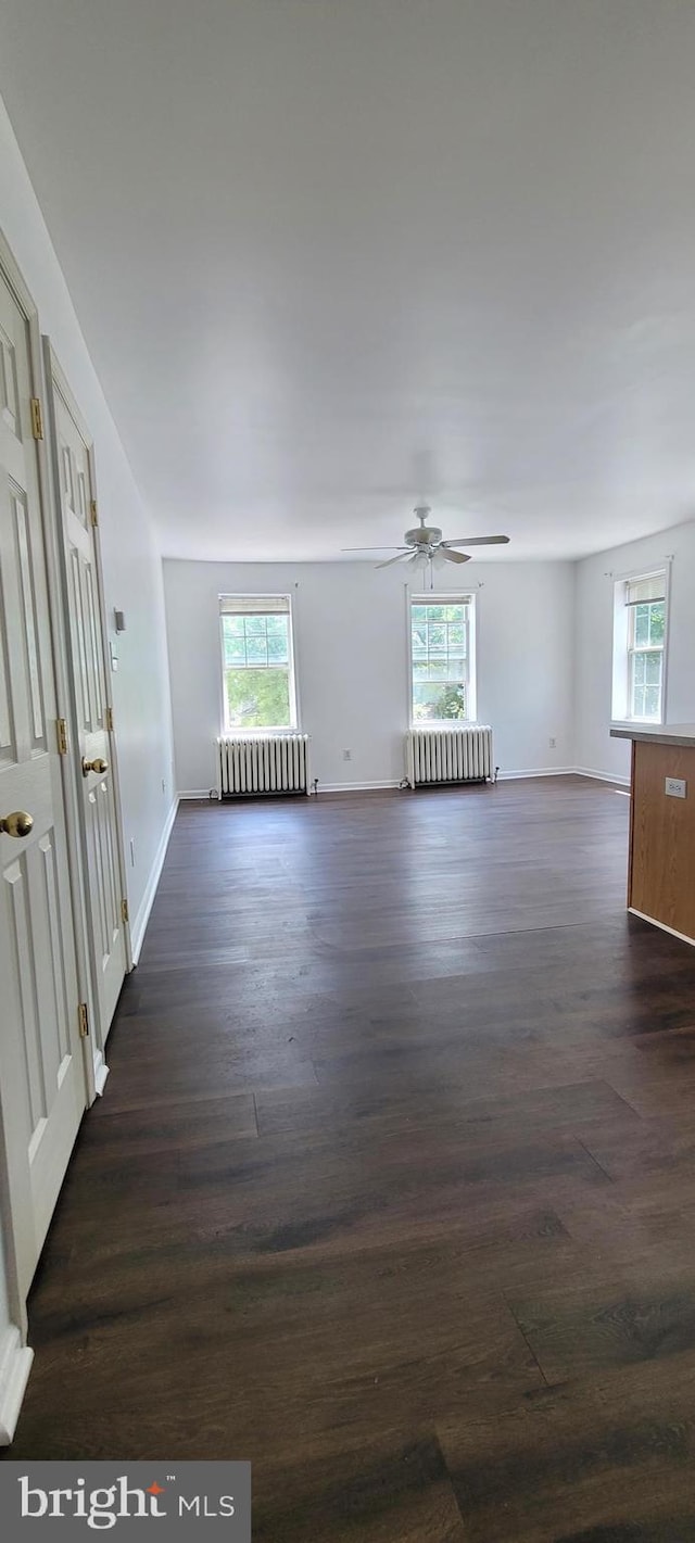 empty room featuring dark hardwood / wood-style floors, ceiling fan, and radiator heating unit