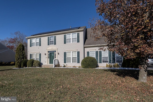 colonial home featuring a front yard and solar panels