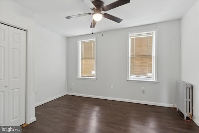 unfurnished bedroom featuring ceiling fan, dark wood-type flooring, radiator, and a closet