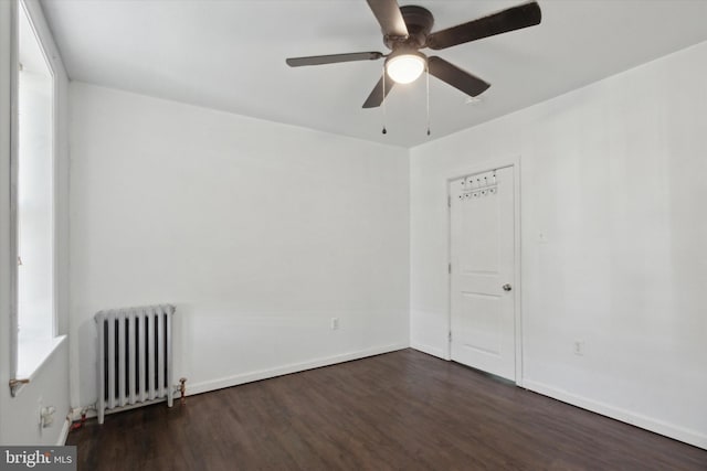 empty room with dark hardwood / wood-style floors, ceiling fan, and radiator