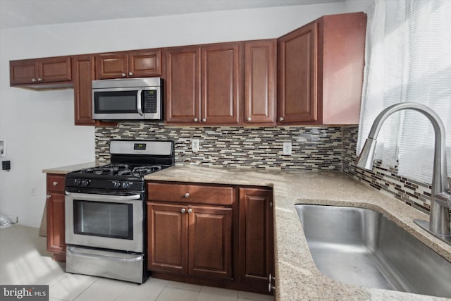 kitchen with appliances with stainless steel finishes, tasteful backsplash, light stone counters, and sink