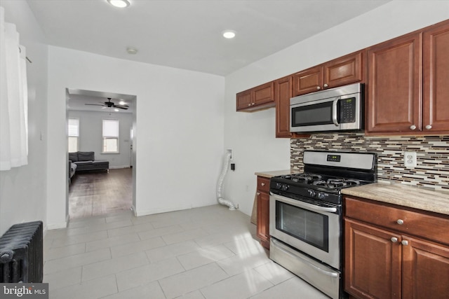 kitchen featuring light stone countertops, appliances with stainless steel finishes, radiator, ceiling fan, and light tile patterned floors