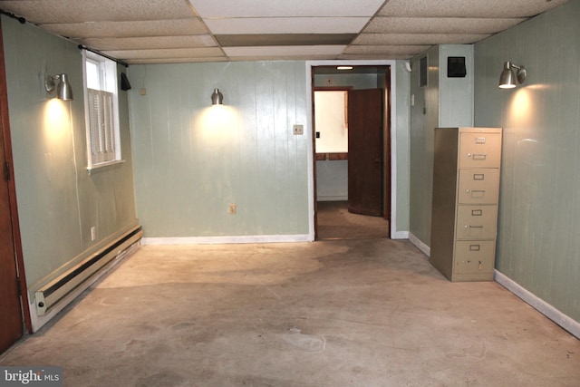 basement featuring wooden walls, a drop ceiling, and a baseboard heating unit