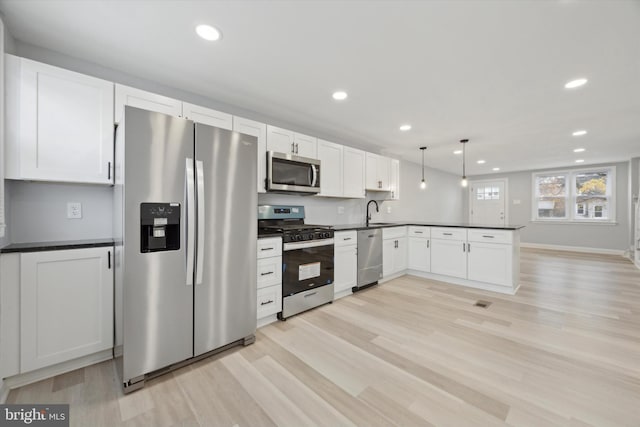 kitchen with appliances with stainless steel finishes, light wood-type flooring, sink, pendant lighting, and white cabinets