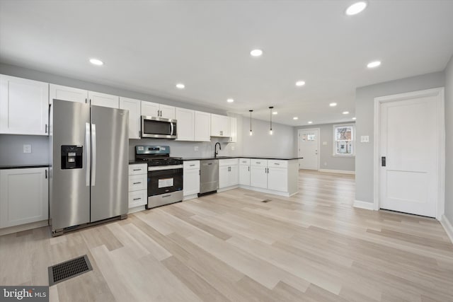 kitchen featuring white cabinetry, sink, hanging light fixtures, appliances with stainless steel finishes, and light wood-type flooring