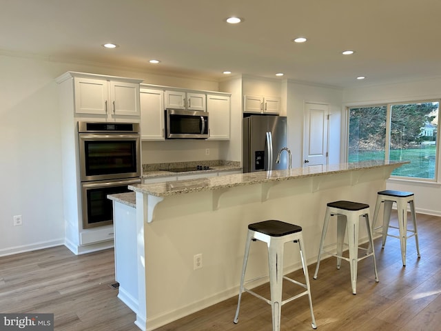 kitchen with a breakfast bar area, white cabinetry, an island with sink, and appliances with stainless steel finishes