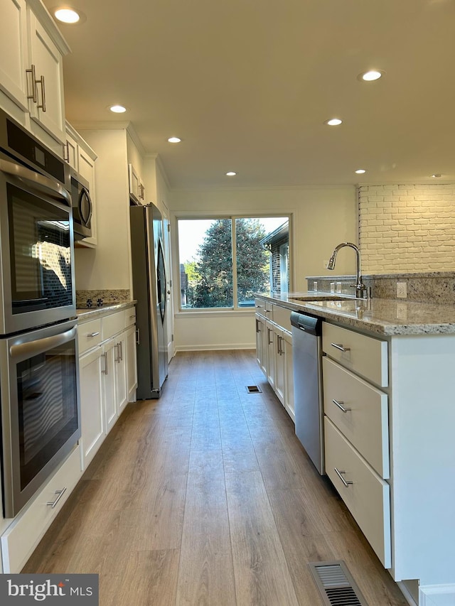 kitchen featuring light stone countertops, stainless steel appliances, white cabinetry, and sink