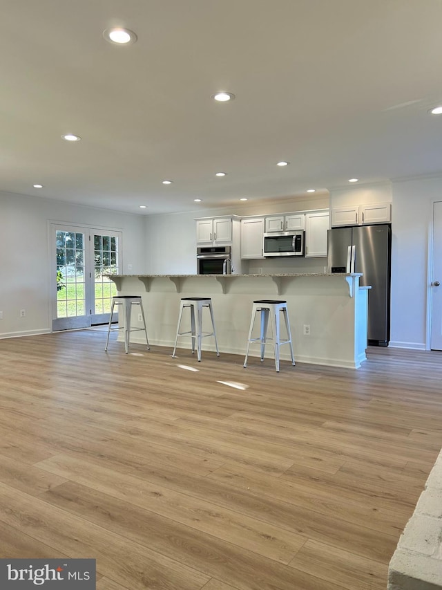 kitchen with light stone countertops, white cabinetry, stainless steel appliances, a kitchen breakfast bar, and light hardwood / wood-style flooring