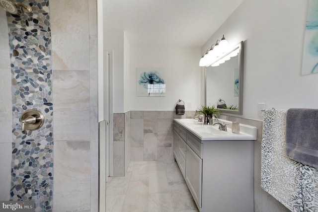 bathroom with a wainscoted wall, a sink, tile walls, a tile shower, and double vanity