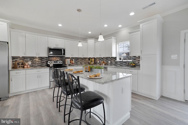 kitchen featuring a center island, light hardwood / wood-style flooring, pendant lighting, white cabinets, and appliances with stainless steel finishes