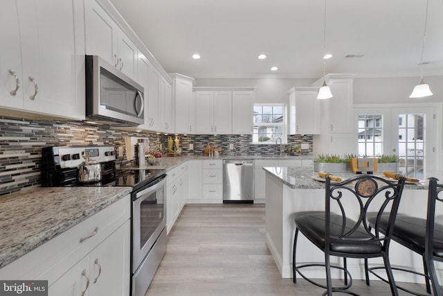 kitchen featuring white cabinets, appliances with stainless steel finishes, decorative backsplash, and a breakfast bar area