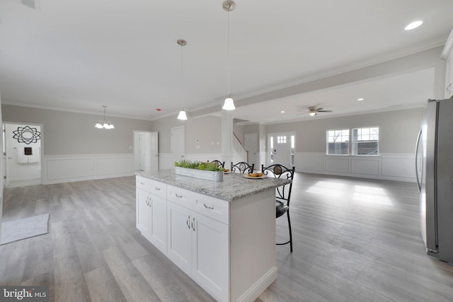 kitchen with stainless steel refrigerator, a center island, hanging light fixtures, light stone counters, and white cabinets