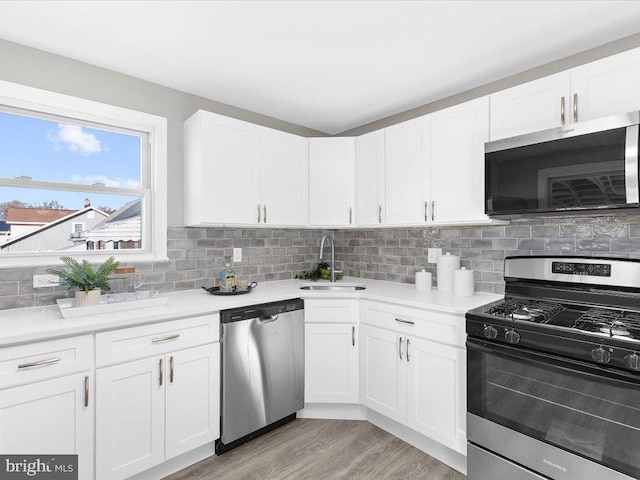 kitchen with appliances with stainless steel finishes, backsplash, sink, white cabinets, and light hardwood / wood-style floors