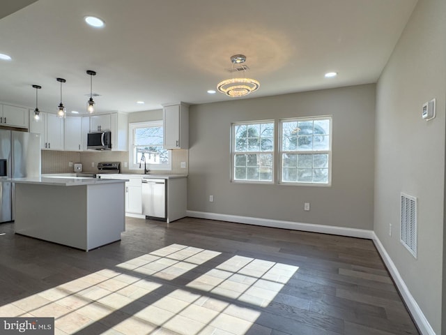 kitchen featuring a center island, dark wood-type flooring, stainless steel appliances, decorative light fixtures, and white cabinets