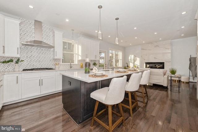 kitchen with a center island with sink, white cabinets, dark hardwood / wood-style floors, and wall chimney range hood