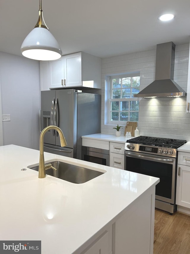 kitchen with white cabinets, wall chimney range hood, sink, and appliances with stainless steel finishes