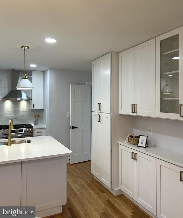 kitchen featuring white cabinets, hardwood / wood-style flooring, wall chimney exhaust hood, high end stove, and decorative light fixtures