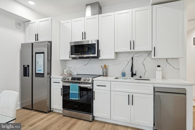 kitchen featuring decorative backsplash, stainless steel appliances, sink, light hardwood / wood-style flooring, and white cabinets