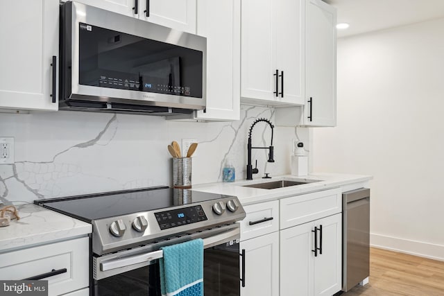 kitchen with white cabinets, sink, appliances with stainless steel finishes, tasteful backsplash, and light hardwood / wood-style floors