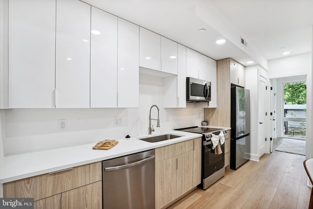 kitchen featuring sink, light brown cabinets, light hardwood / wood-style floors, white cabinets, and appliances with stainless steel finishes