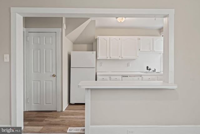 kitchen featuring sink, kitchen peninsula, white appliances, white cabinets, and light wood-type flooring