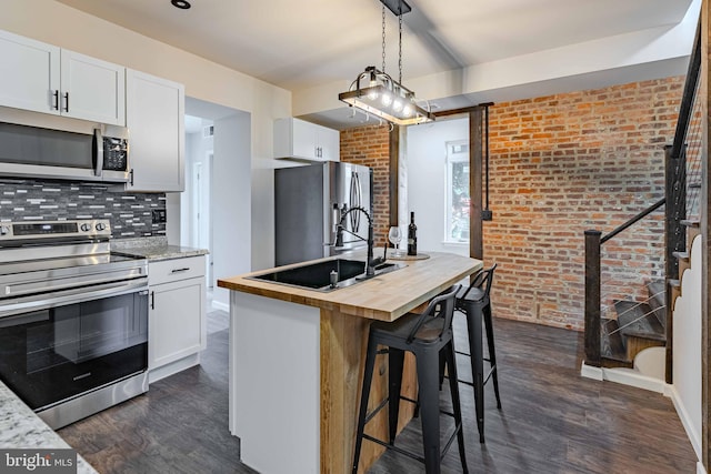 kitchen with white cabinets, brick wall, a center island with sink, and appliances with stainless steel finishes