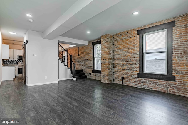 unfurnished living room with a healthy amount of sunlight, brick wall, and dark hardwood / wood-style floors