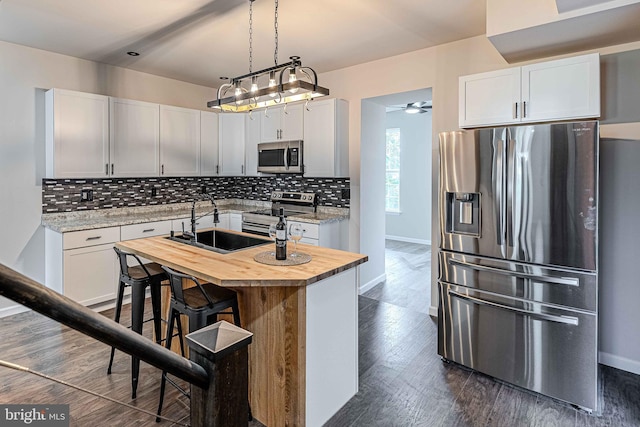 kitchen with appliances with stainless steel finishes, dark hardwood / wood-style flooring, a center island with sink, and white cabinetry