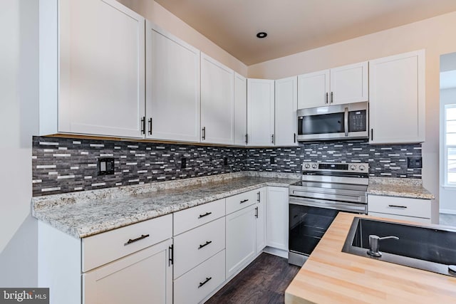 kitchen with light stone countertops, stainless steel appliances, dark hardwood / wood-style floors, backsplash, and white cabinets