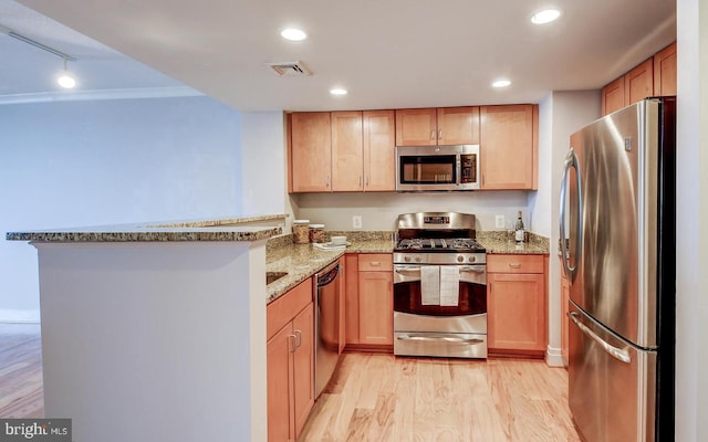 kitchen with kitchen peninsula, appliances with stainless steel finishes, rail lighting, light stone counters, and light hardwood / wood-style floors