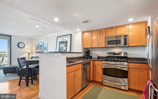 kitchen with kitchen peninsula, stainless steel appliances, dark stone counters, and light hardwood / wood-style flooring