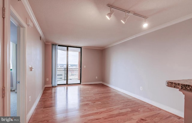 unfurnished room featuring light wood-type flooring, track lighting, a wall of windows, and crown molding