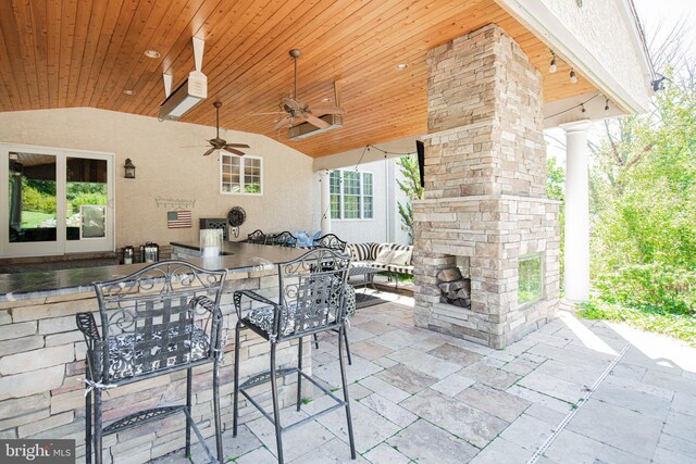 view of patio featuring exterior bar, ceiling fan, and an outdoor stone fireplace