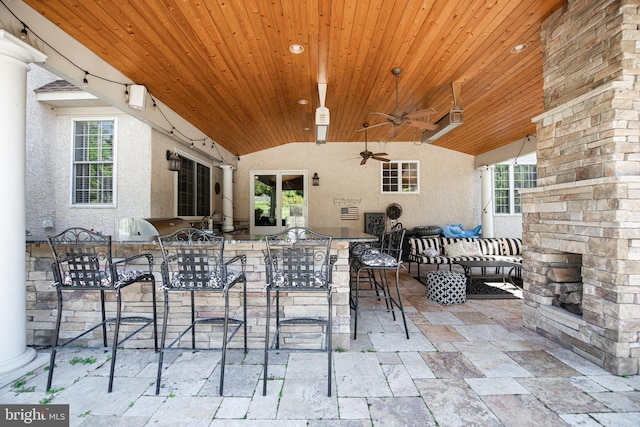 view of patio with ceiling fan, exterior bar, exterior kitchen, and a fireplace