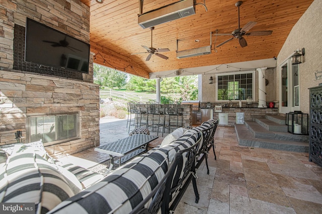 view of patio featuring exterior bar, exterior kitchen, an outdoor living space with a fireplace, and ceiling fan