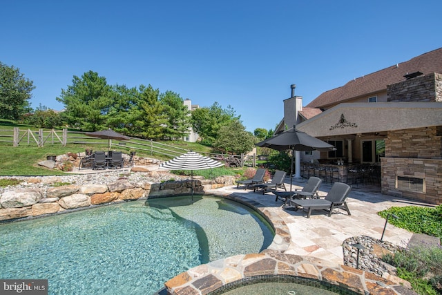 view of pool with a patio, a bar, an outdoor stone fireplace, and an outdoor fire pit