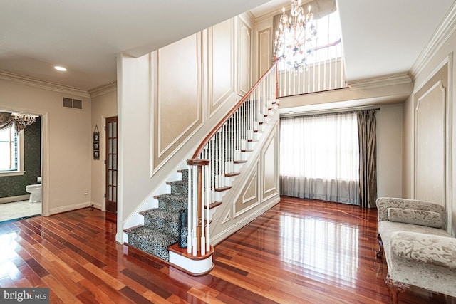 stairs featuring hardwood / wood-style flooring, crown molding, and a notable chandelier