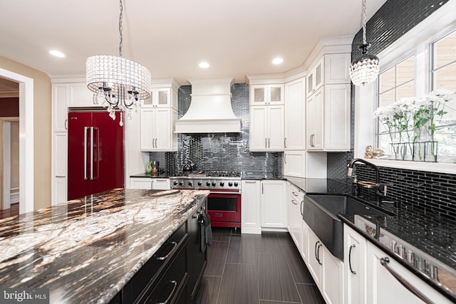 kitchen with range, hanging light fixtures, premium range hood, high end fridge, and white cabinetry