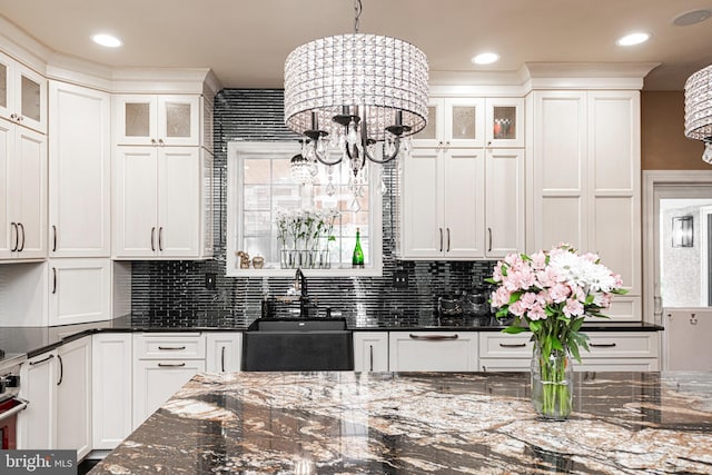 kitchen featuring white cabinetry, decorative light fixtures, sink, dark stone counters, and a chandelier