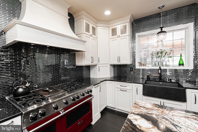 kitchen featuring sink, custom range hood, range with two ovens, decorative backsplash, and pendant lighting