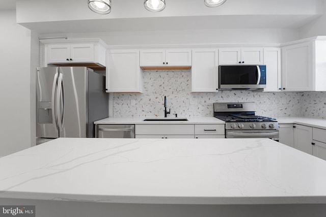 kitchen with light stone countertops, appliances with stainless steel finishes, white cabinetry, sink, and backsplash