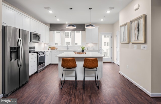 kitchen with appliances with stainless steel finishes, decorative light fixtures, a kitchen island, and dark wood-type flooring