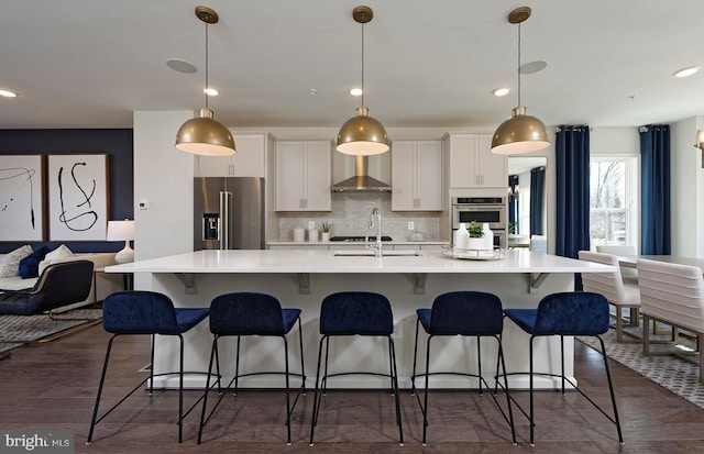 kitchen with pendant lighting, a large island, wall chimney exhaust hood, and appliances with stainless steel finishes